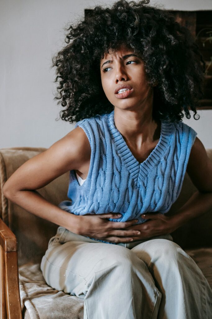 pexels-photo-5938354-5938354 Young African American female sitting on couch at home while having acute pain in stomach